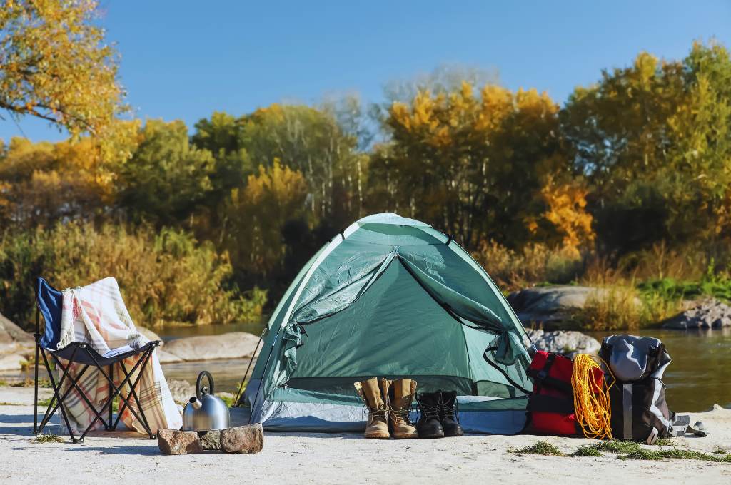 camping essentials and equipment near camping tent at lake shore